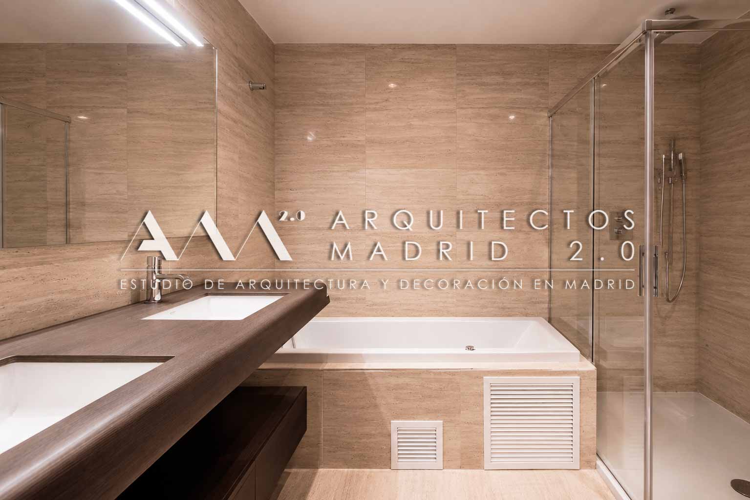 Baño terminado con revestimiento de travertino, doble lavabo, bañera y ducha en vivienda de Trafalgar, Chamberí