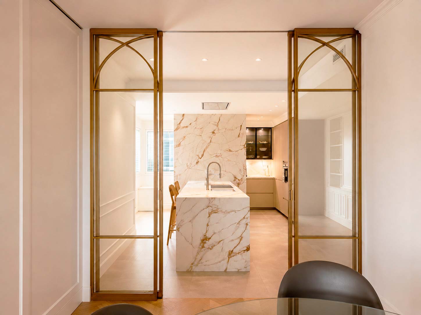 Cocina abierta hacia el comedor mediante puertas acristaladas de acero lacado en bronce en vivienda reformada de Fuencarral, Chamberí