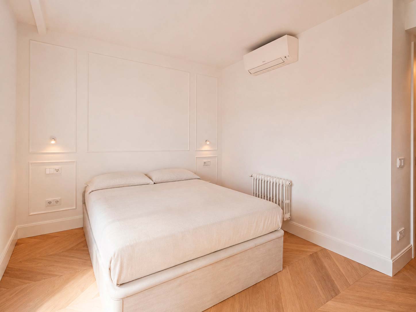 Dormitorio principal con parquet en espiga, molduras e iluminación integrada en la reforma de Fuencarral, Chamberí