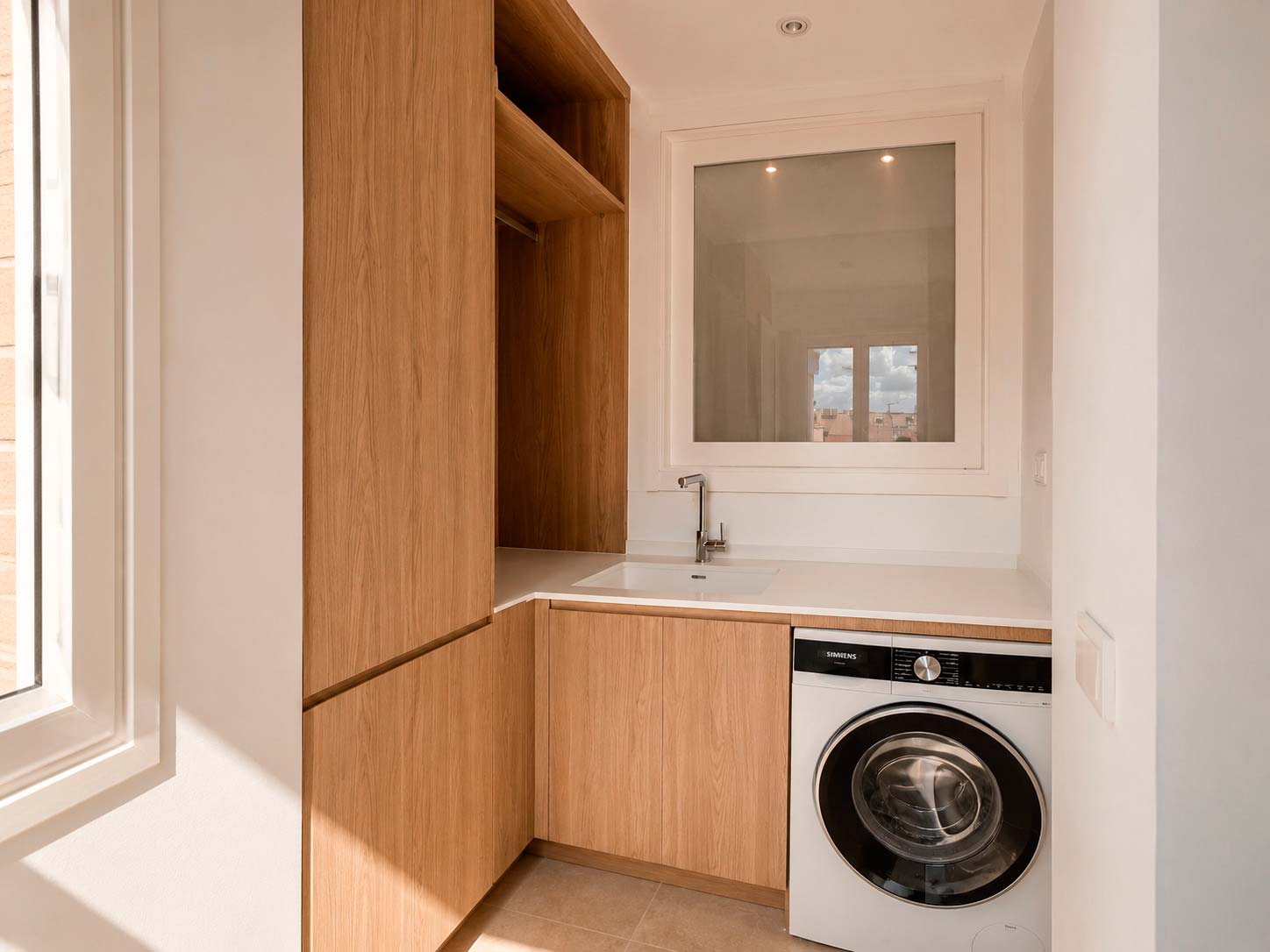 Lavadero integrado con mobiliario de madera diseñado a medida dentro de la cocina de la vivienda reformada en Fuencarral