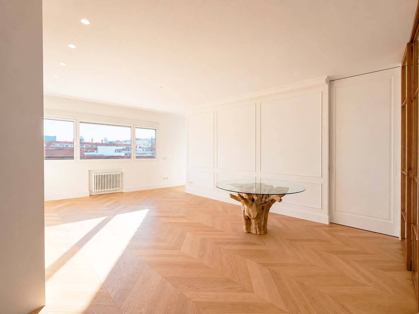 Salón luminoso con parquet de madera en espiga y paredes con molduras tras la reforma integral de una vivienda en la calle Fuencarral, Chamberí