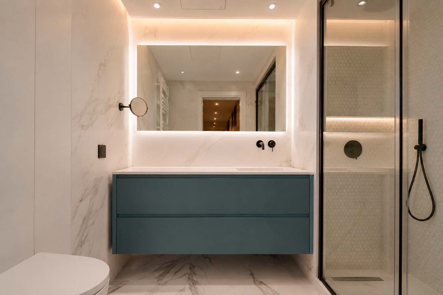 Baño con mueble suspendido azul, espejo retroiluminado y ducha con grifería negra en vivienda reformada en calle Orense, Madrid