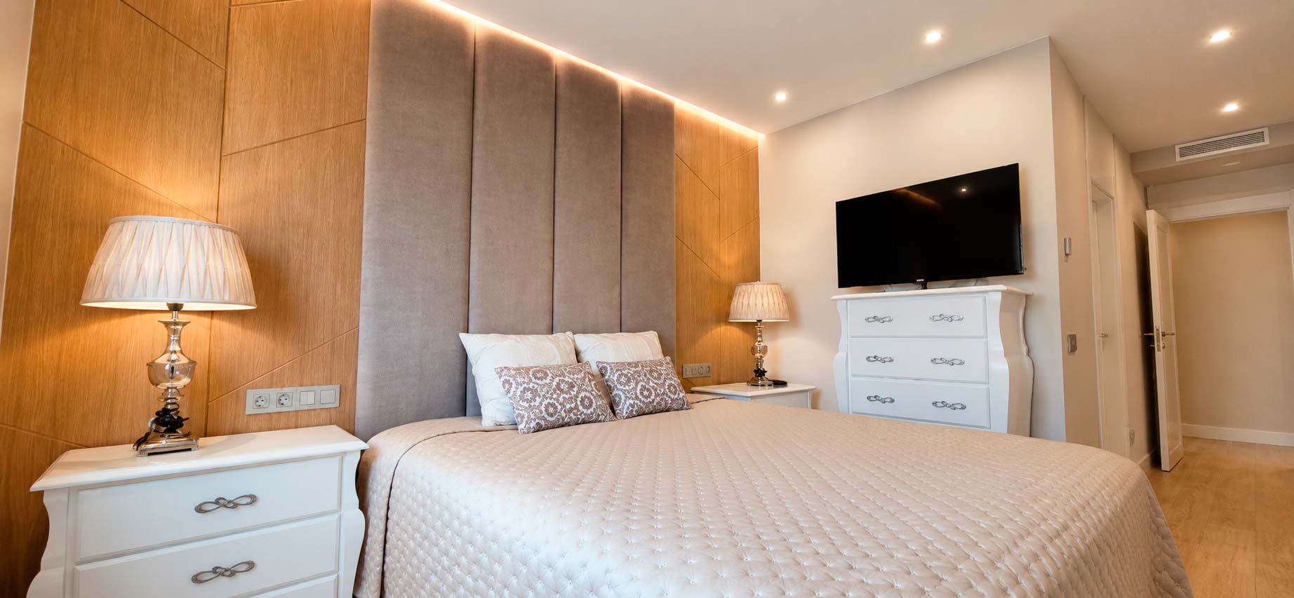 Dormitorio principal con cabecero de madera, paneles tapizados e iluminación LED integrada en ático dúplex reformado en calle Orense, Madrid