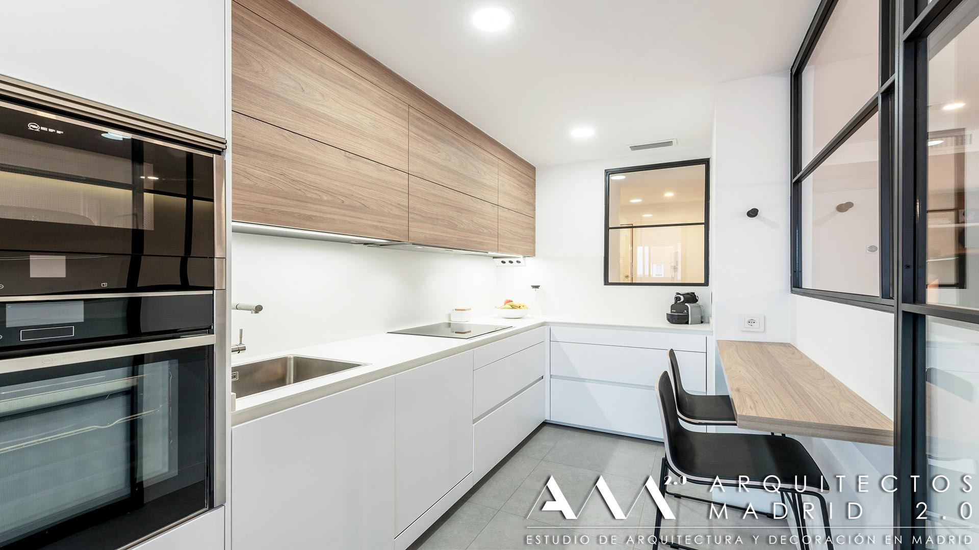 Cocina blanca y madera con barra de desayunos y cerramiento acristalado en vivienda reformada de Las Rosas, Madrid