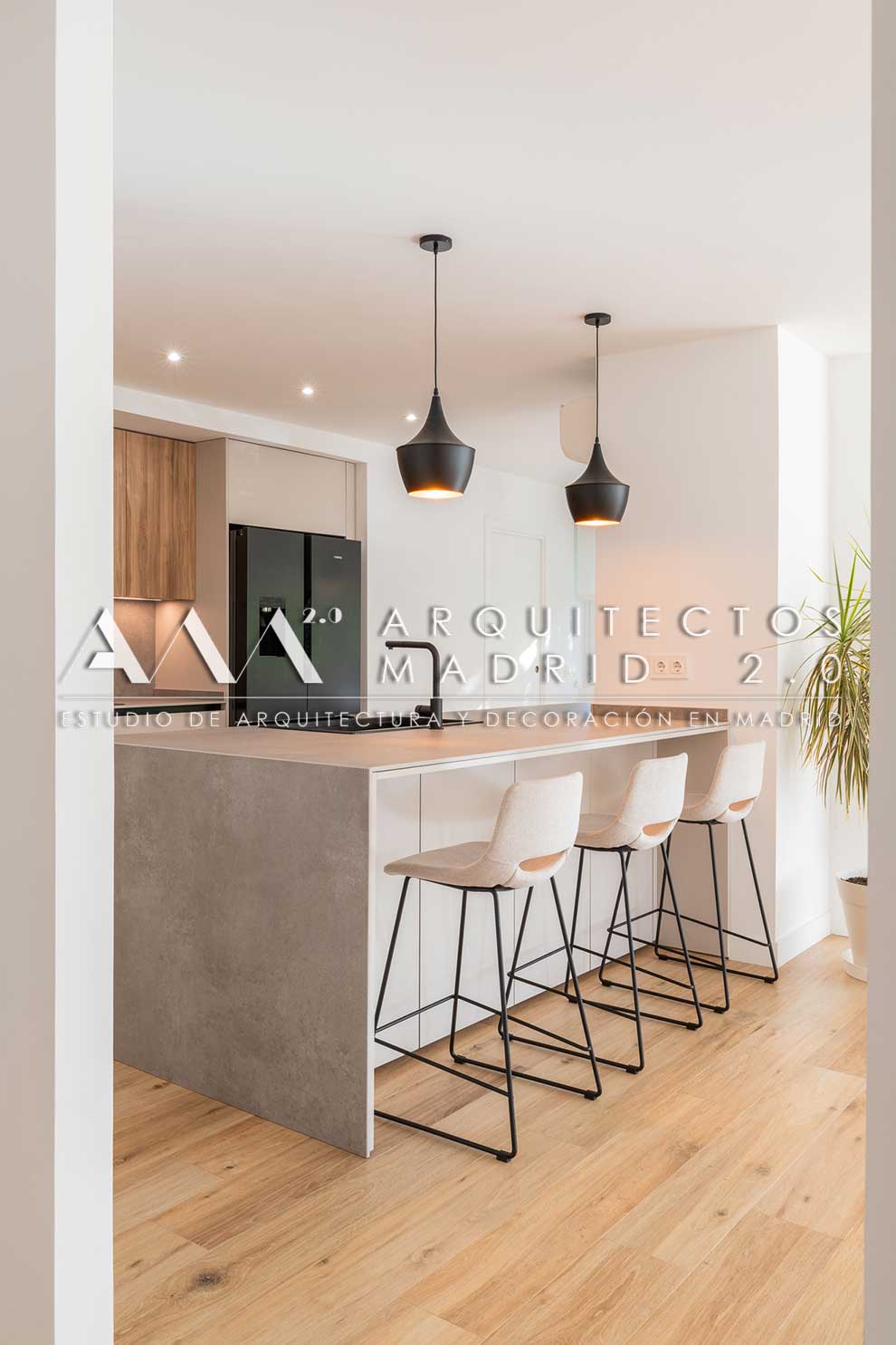Isla de cocina con acabado mineral, taburetes blancos y lámparas negras en vivienda familiar reformada en Chamartín