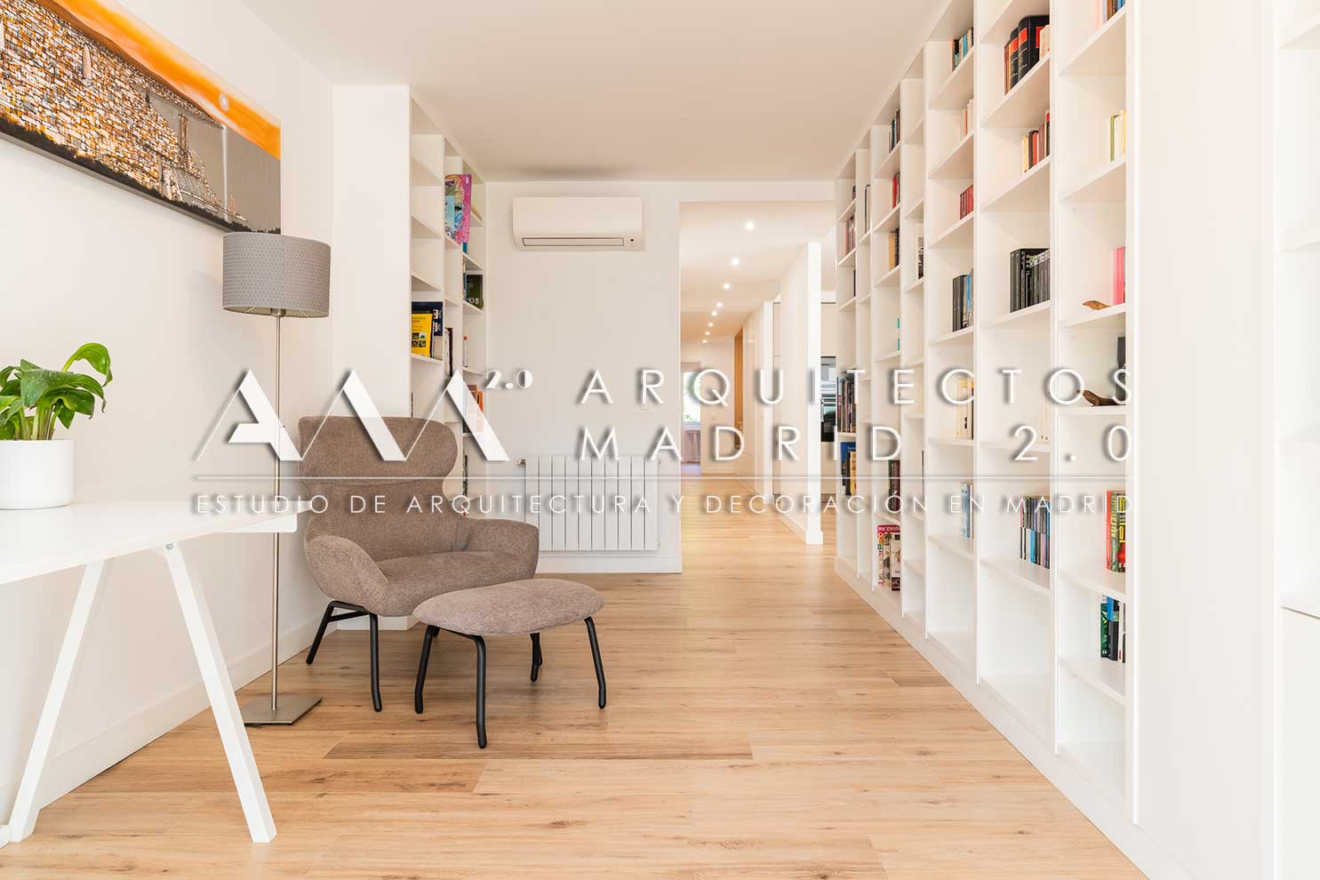 Zona de lectura integrada en el pasillo con biblioteca blanca y pavimento continuo de madera