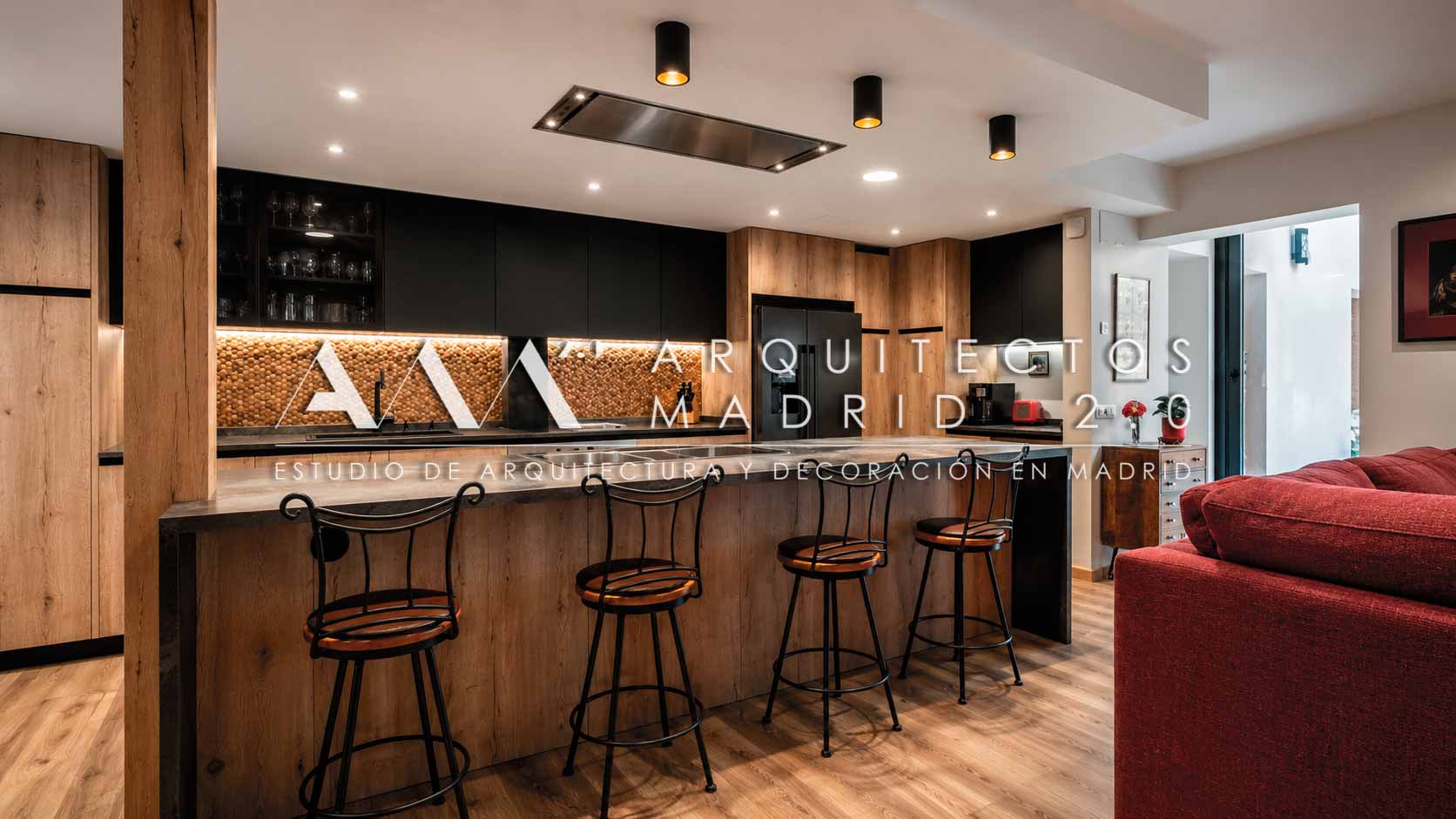 Cocina con isla negra, madera y luminarias cilíndricas en vivienda unifamiliar rehabilitada en Madrid